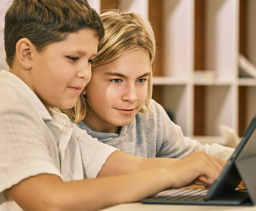 Zwei Schülerinnen sitzen vor zwei Tablets und lachen